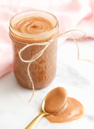 A jar of homemade caramel with a giolden spoon in the foreground.