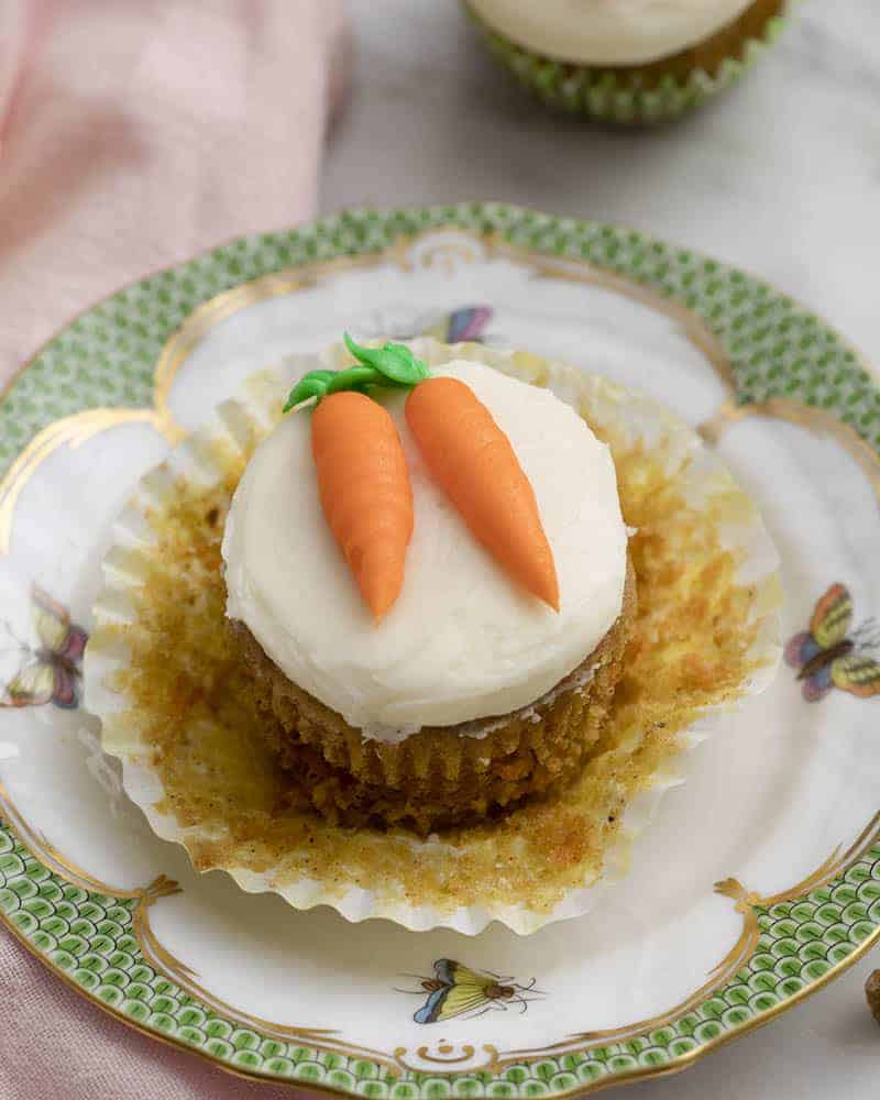 An unwrapped carrot cake cupcake topped with two buttercream carrots on a plate.