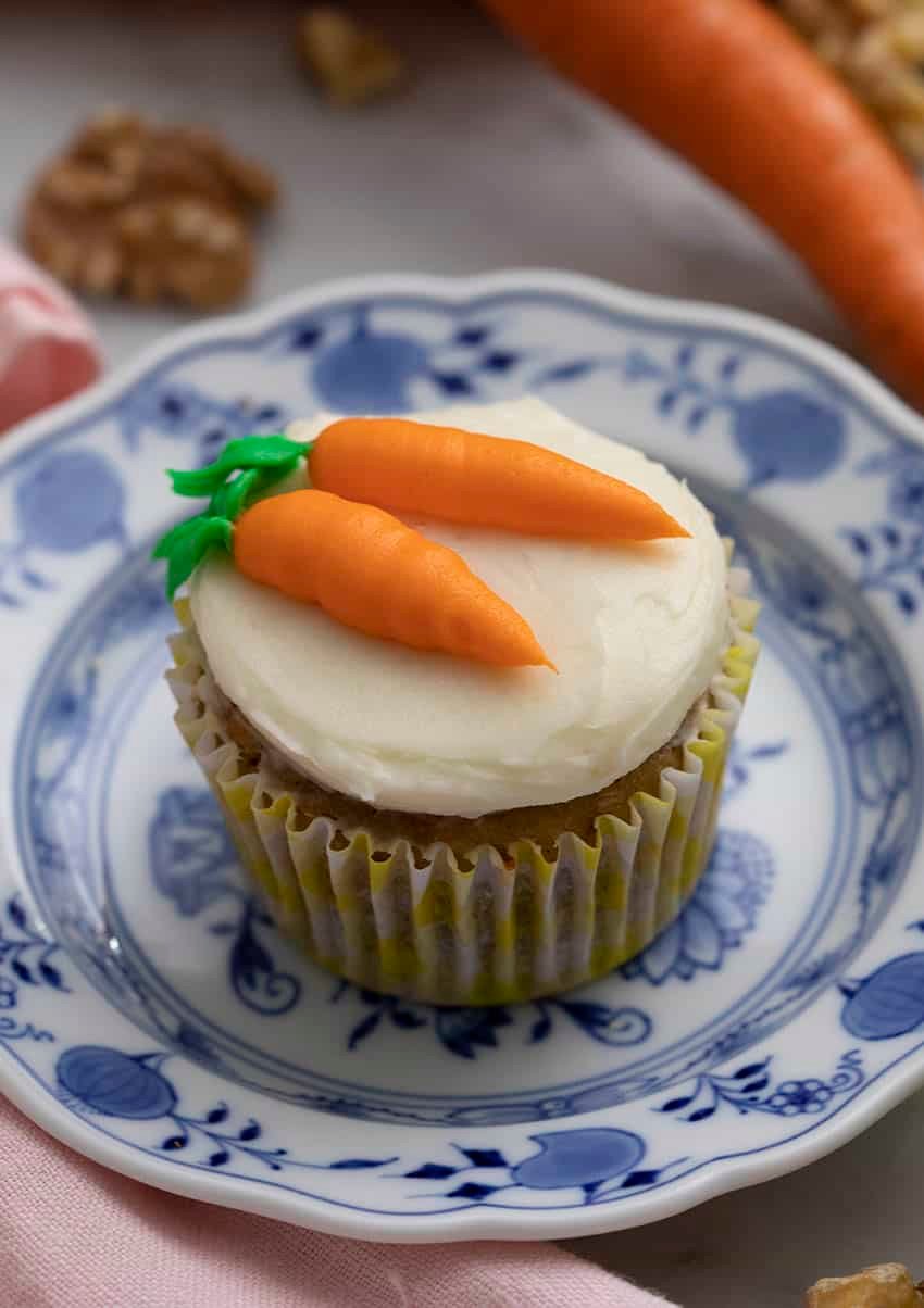 A carrot cake cupcake with two buttercream carrots piped on top.