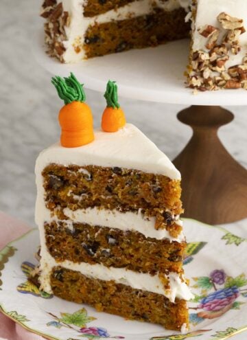 A big three layer carrot cake with a piece in the foreground.