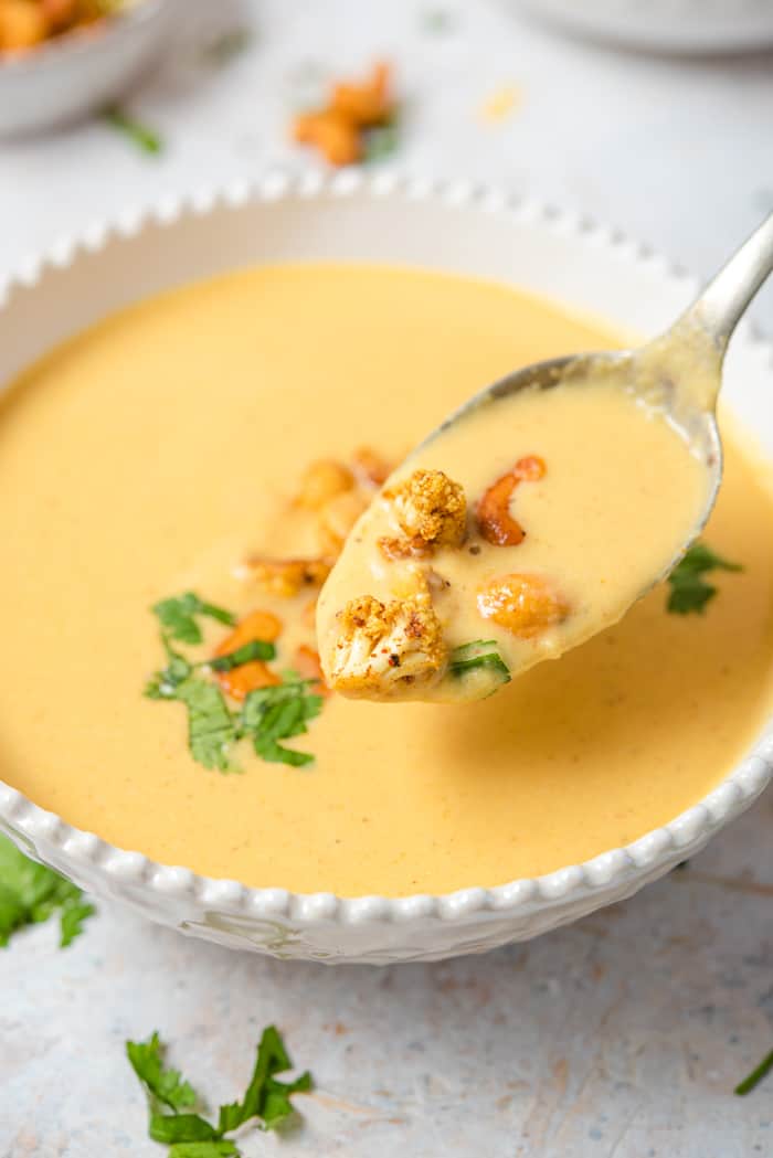 A spoonful of soup topped with cauliflower and cashews