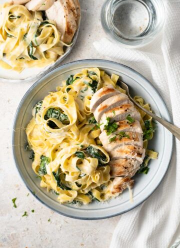 An overhead shot of chicken alfredo with spinach in a blue bowl