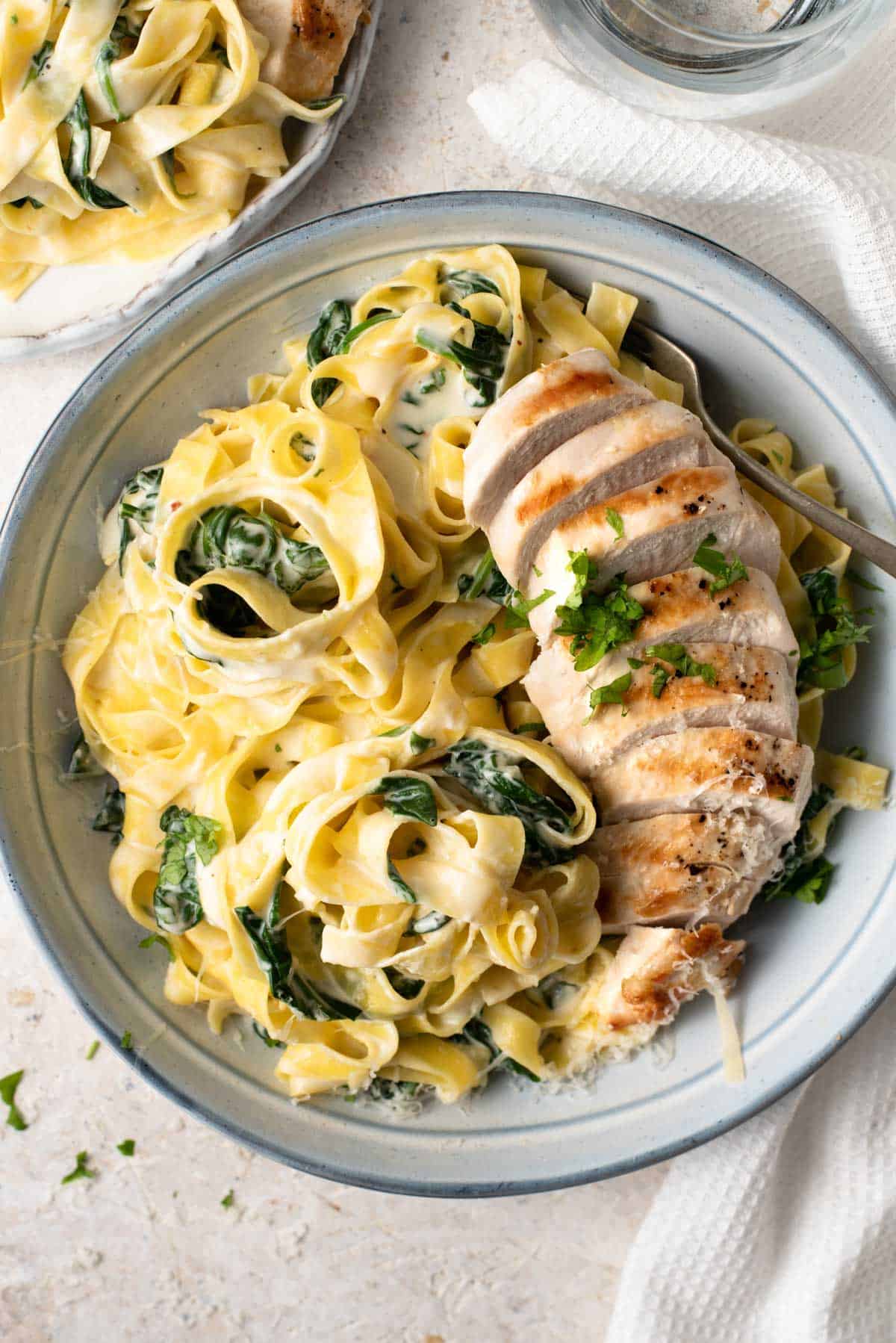 A close up of chicken alfredo in a bowl topped with parsley
