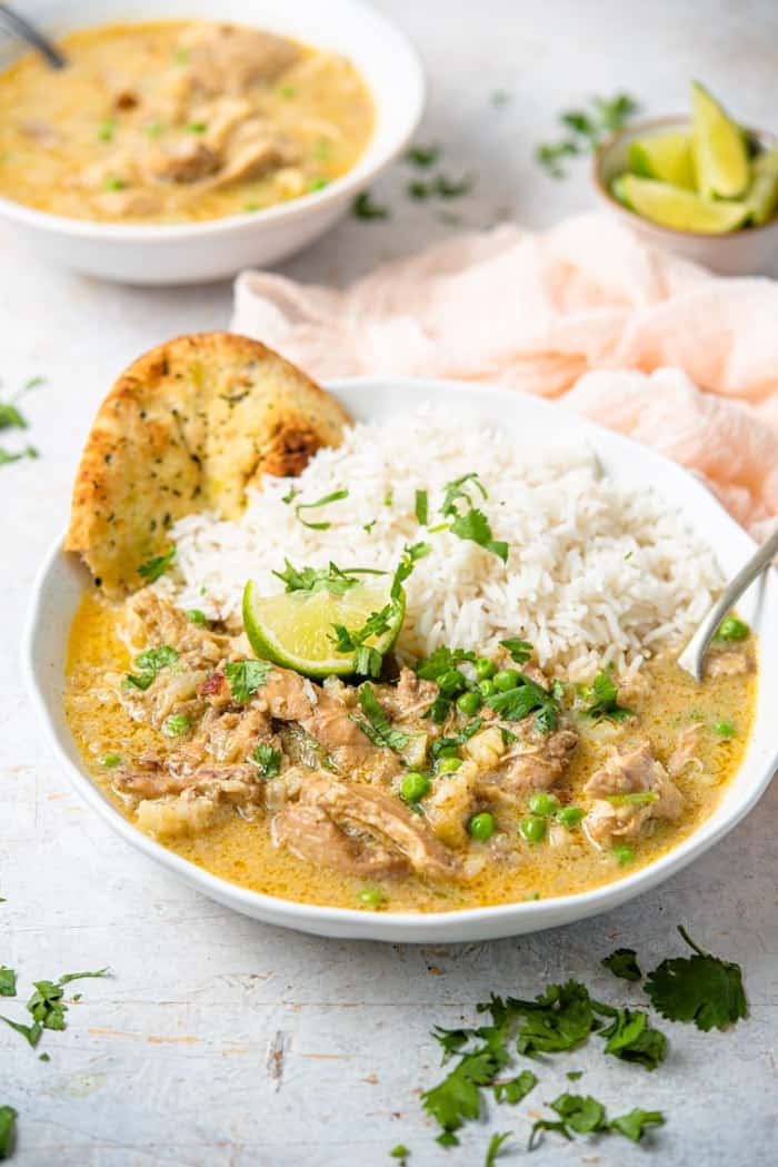 A side shot of chicken curry in a bowl with rice and naan bread