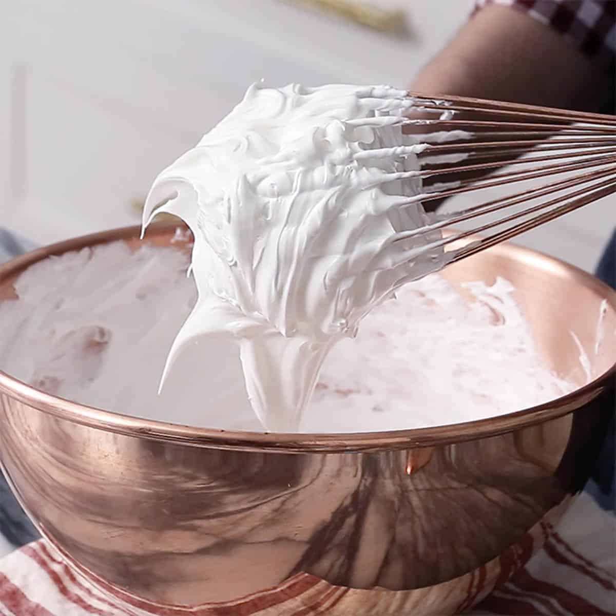 Meringue whipped to stiff peaks in a copper bowl.