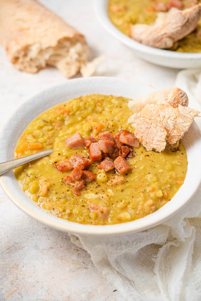 A side shot of split pea soup in a bowl topped with cooked ham