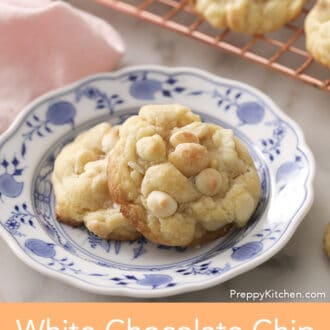 Two white chocolate chip macadamia nut cookies on a blue and white plate.