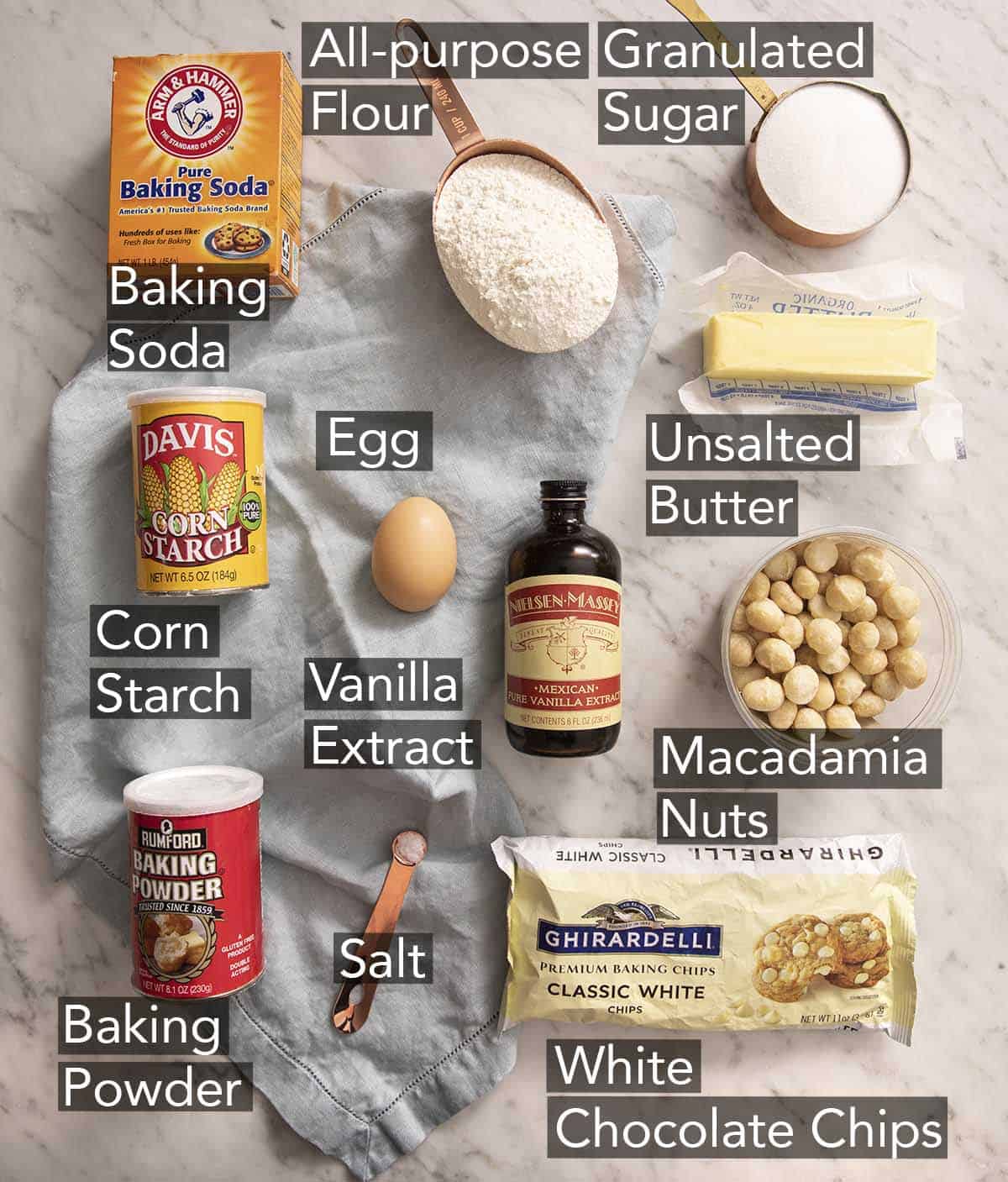 Ingredients to make white chocolate chip macadamia nut cookies on a marble counter.