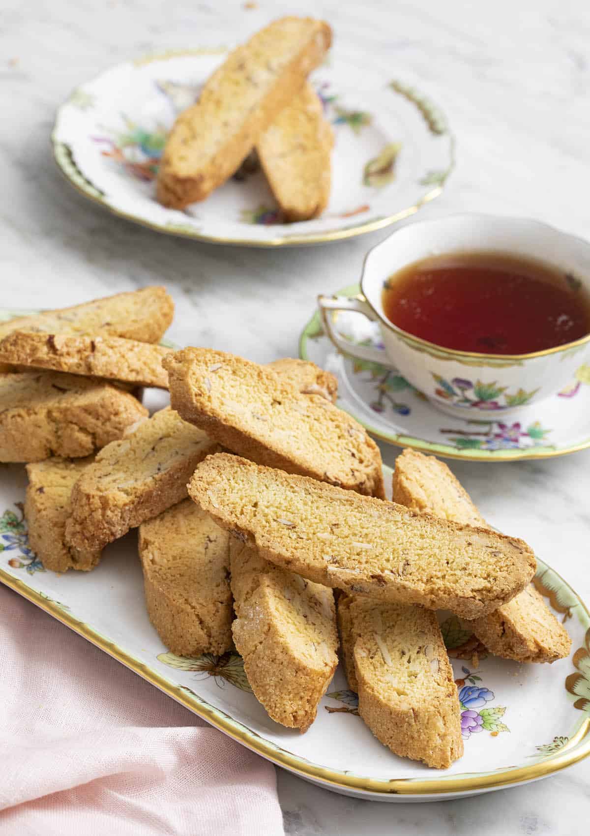A group of delicious almond biscotti on a porcelain serving tray next to a teacup.