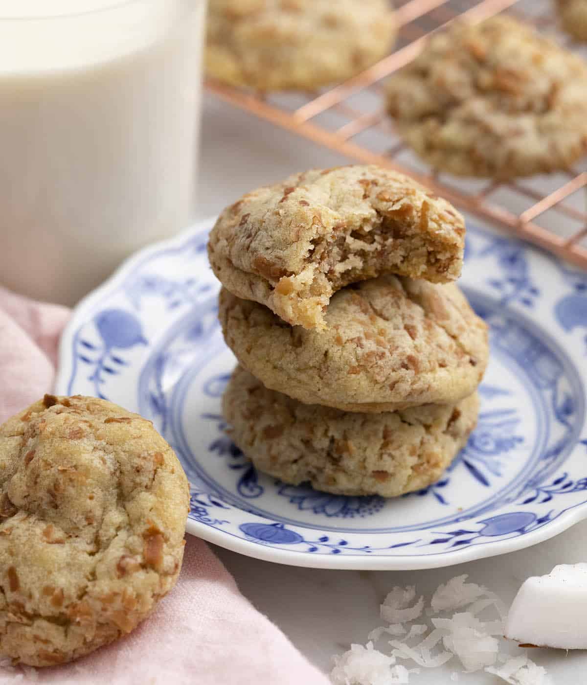 A stack of three coconut cookies on a plate. The top one has a bite taken out.