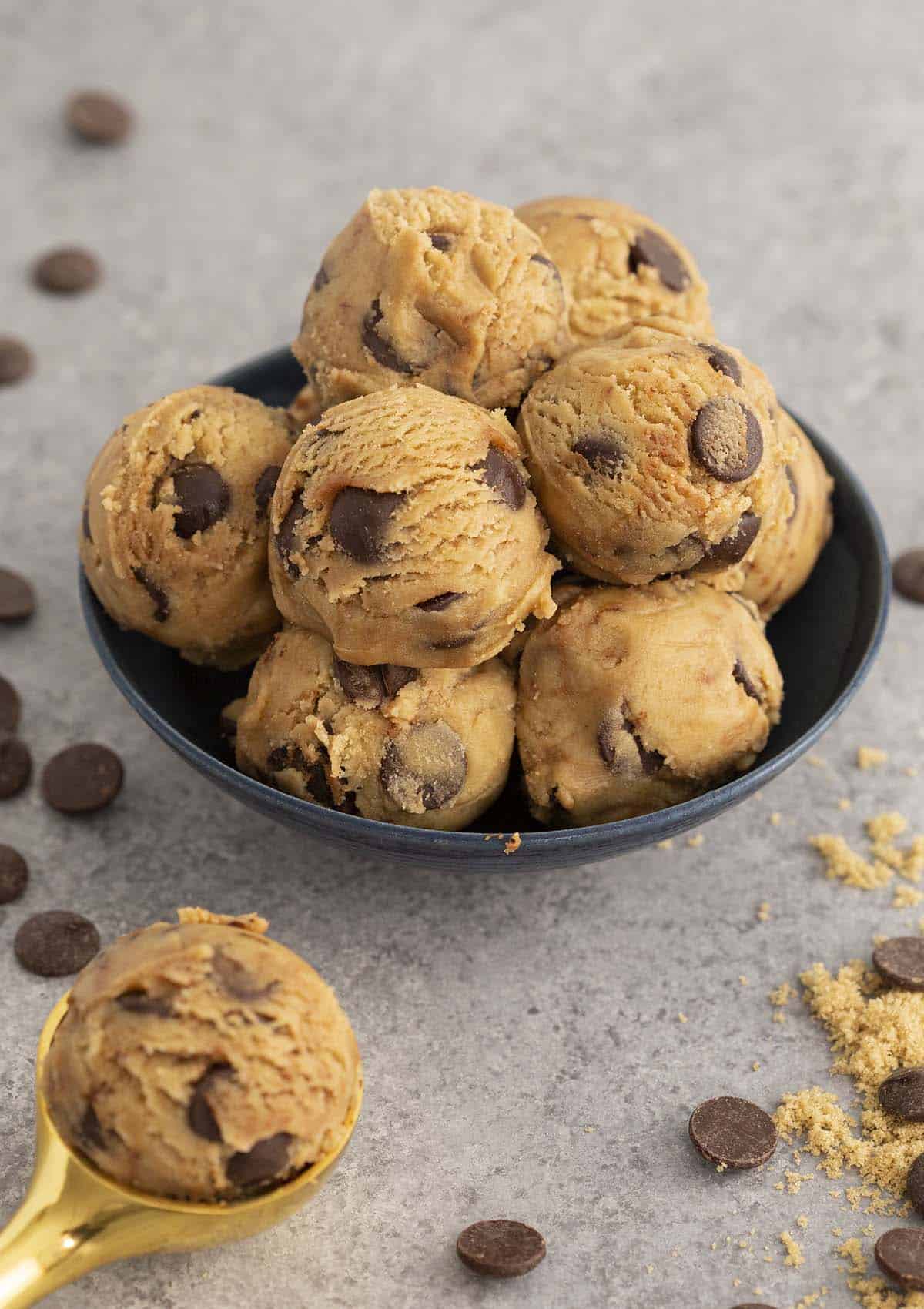 Chocolate chip cookie dough in a bowl with a spoonful in front.