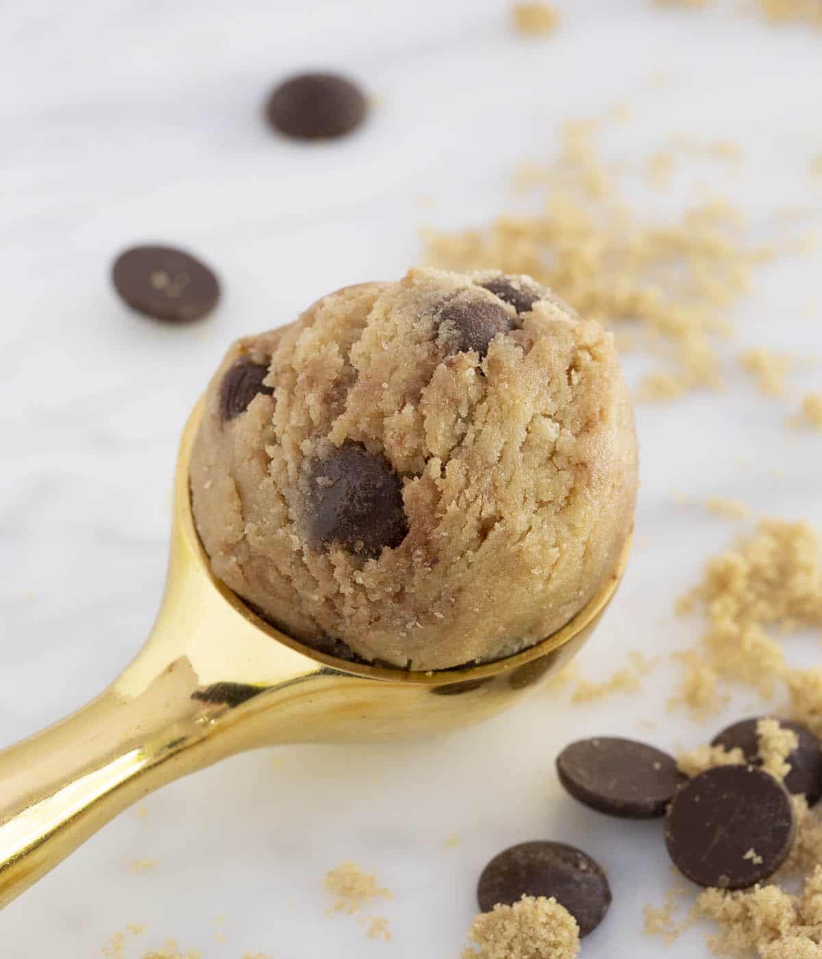 A gold ice cream scoop holding chocolate chip cookie dough with chocolate chips scattered around.