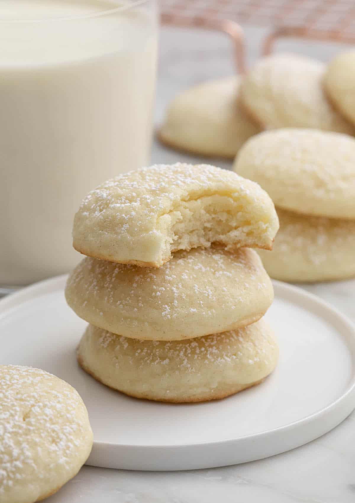 Cream cheese cookies stacked next to a glass of milk.