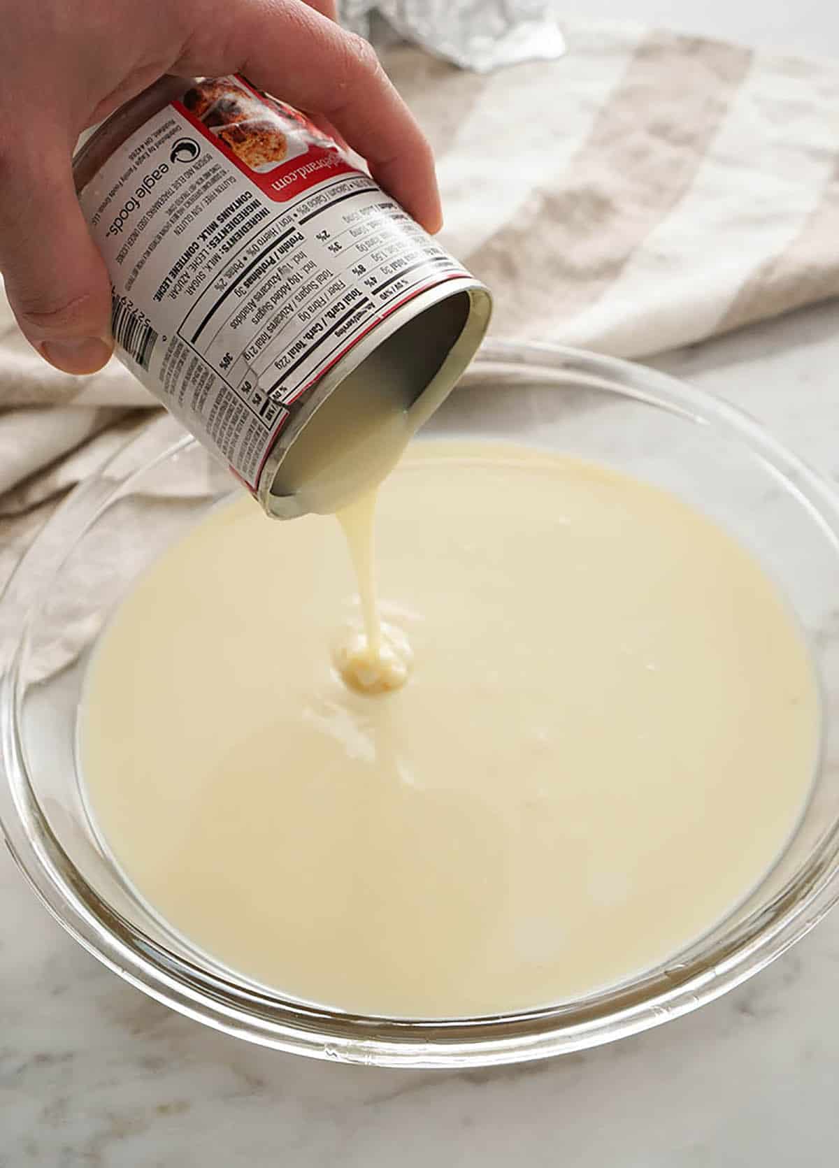 Sweetened condensed milk getting poured into a pie dish.