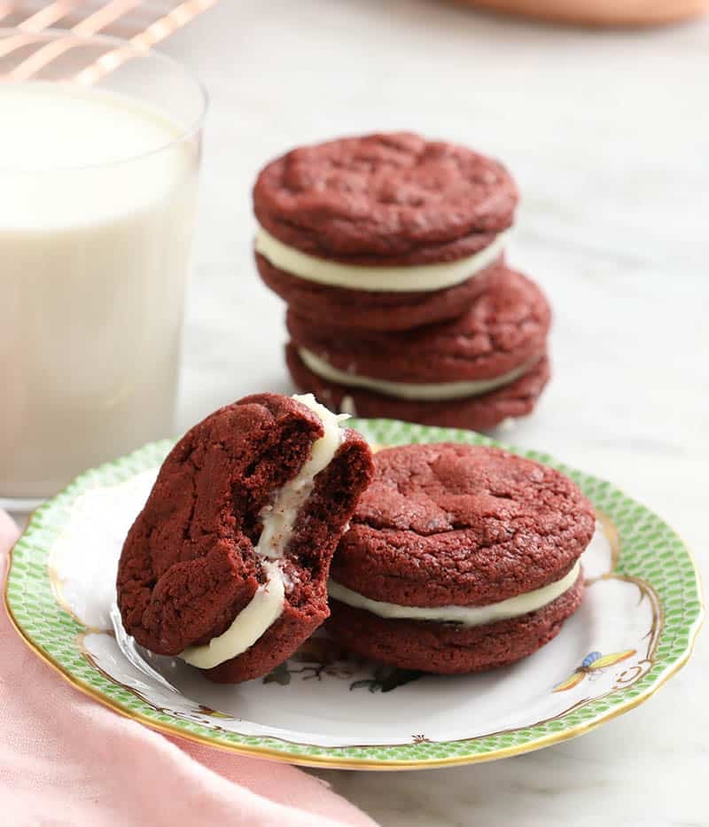 A group of red velvet cookie on a plate with one having a bite taken out.