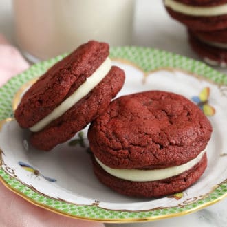 Two red velvet cookies next to a glass of milk.