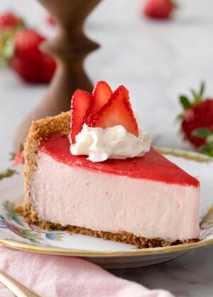 A piece of no bake strawberry cheesecake topped with a pink reduction and whipped cream on a porcelain plate.