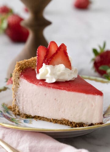 A piece of no bake strawberry cheesecake topped with a pink reduction and whipped cream on a porcelain plate.