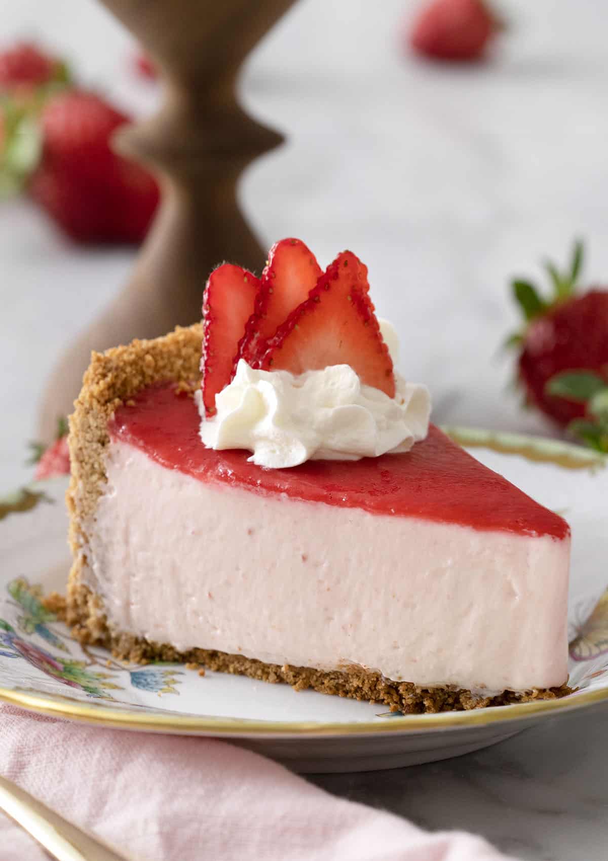 A piece of no bake strawberry cheesecake topped with a pink reduction and whipped cream on a porcelain plate.