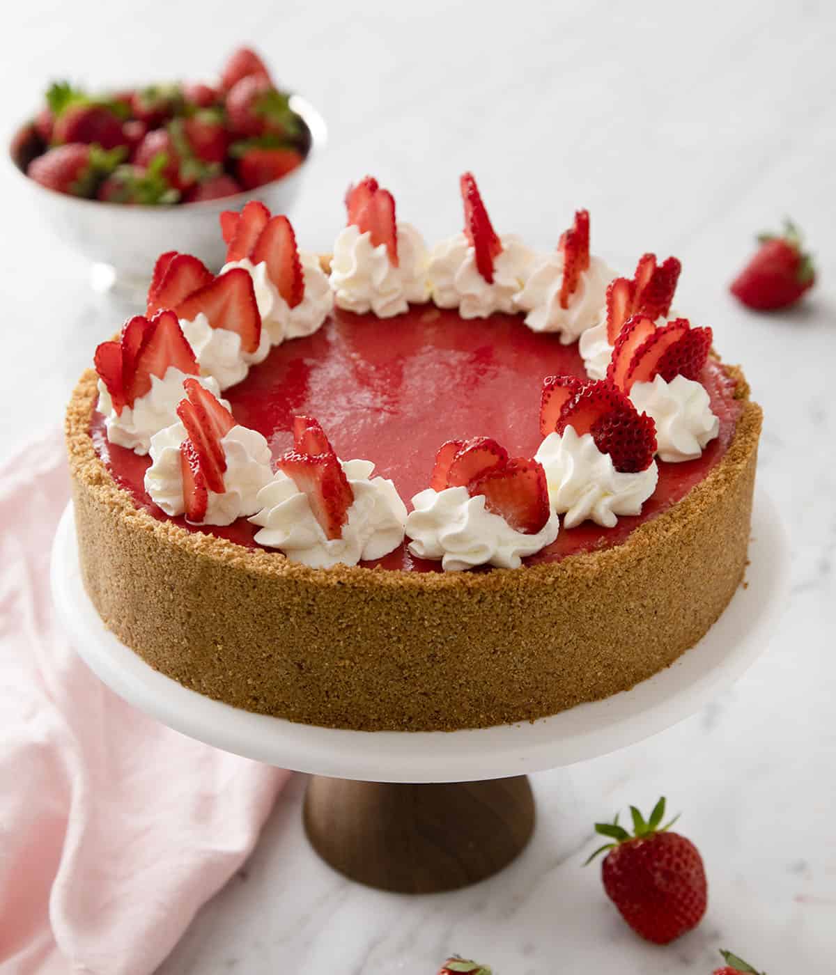 A no bake strawberry cheesecake on a cake stand ready to be cut and served.