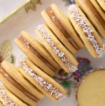 Alfajores on a porcelain serving tray, with every other one rolled in coconut.