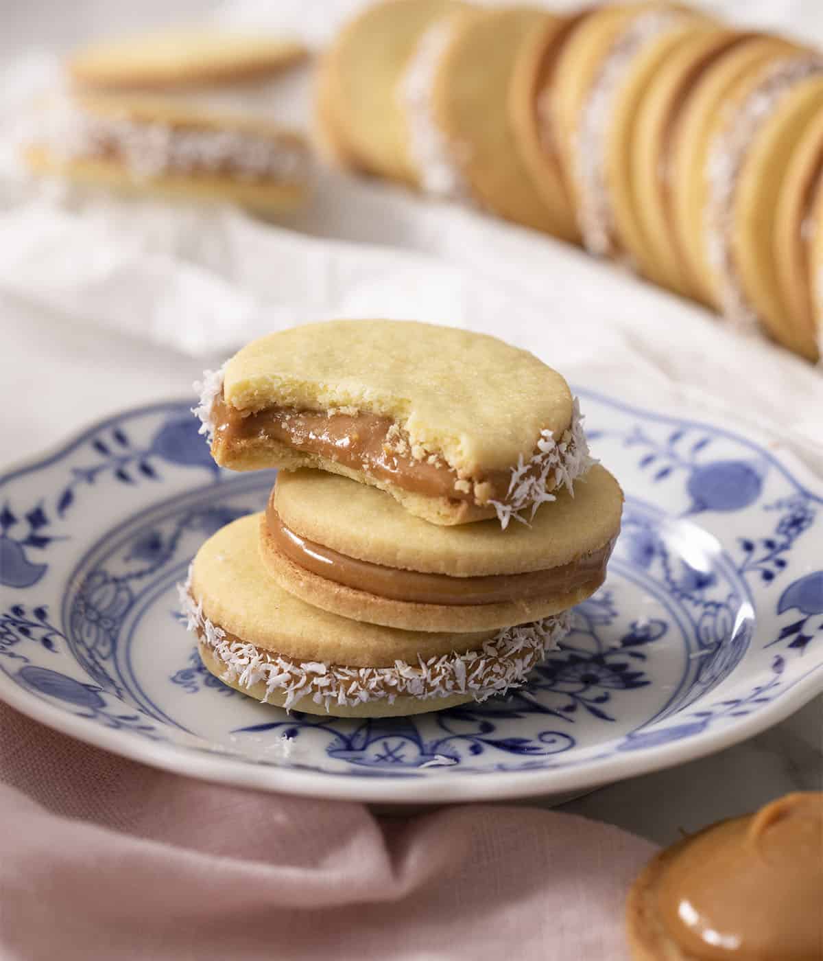 Three alfajores cookies on a plate; the top one has a bite taken out. 