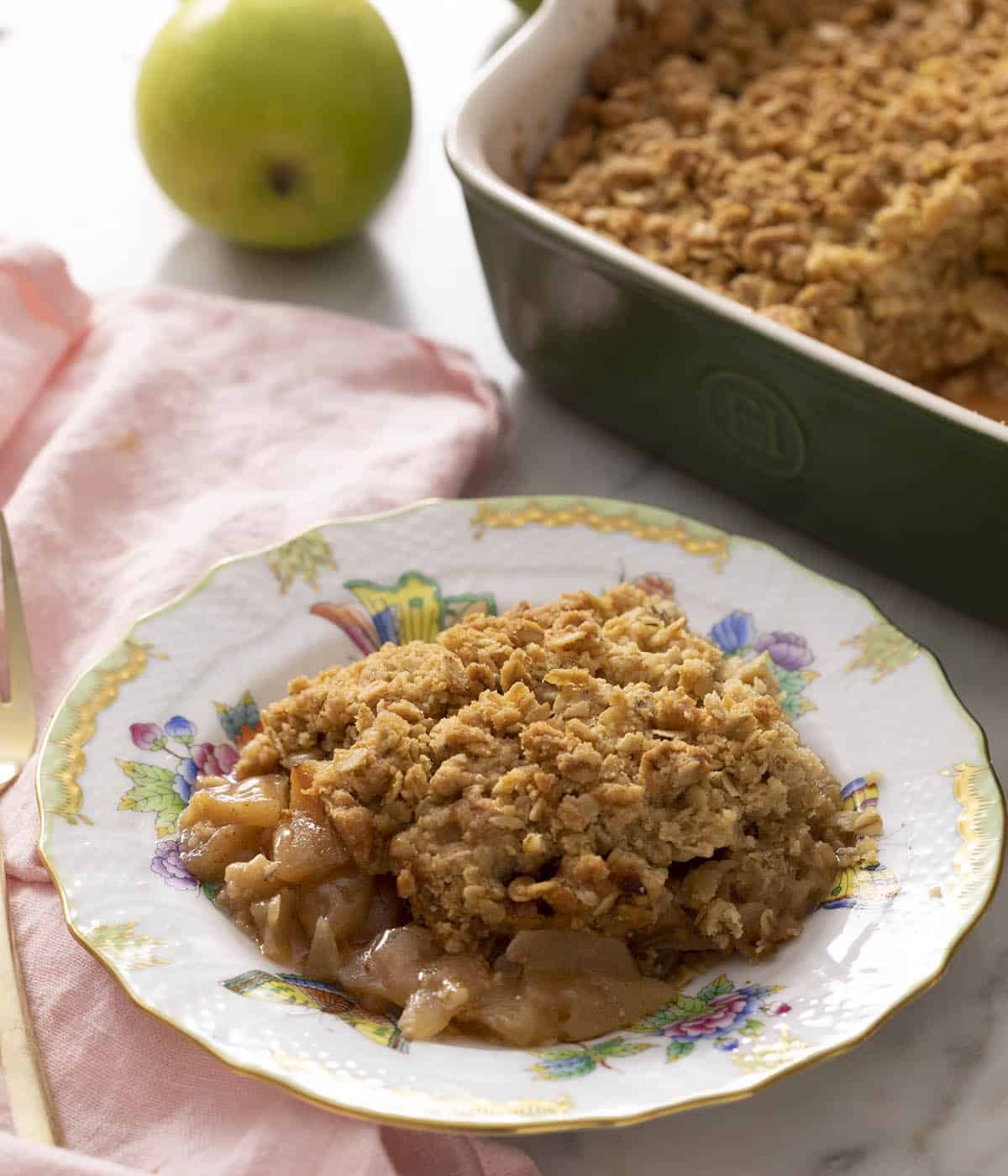 Apple crisp on a plate ready to eat. A baking dish with more apple crisp in the background.