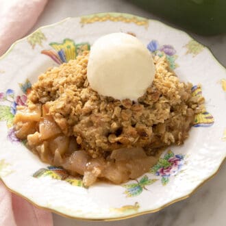 A piece of apple crisp topped with vanilla ice cream on a porcelain plate.