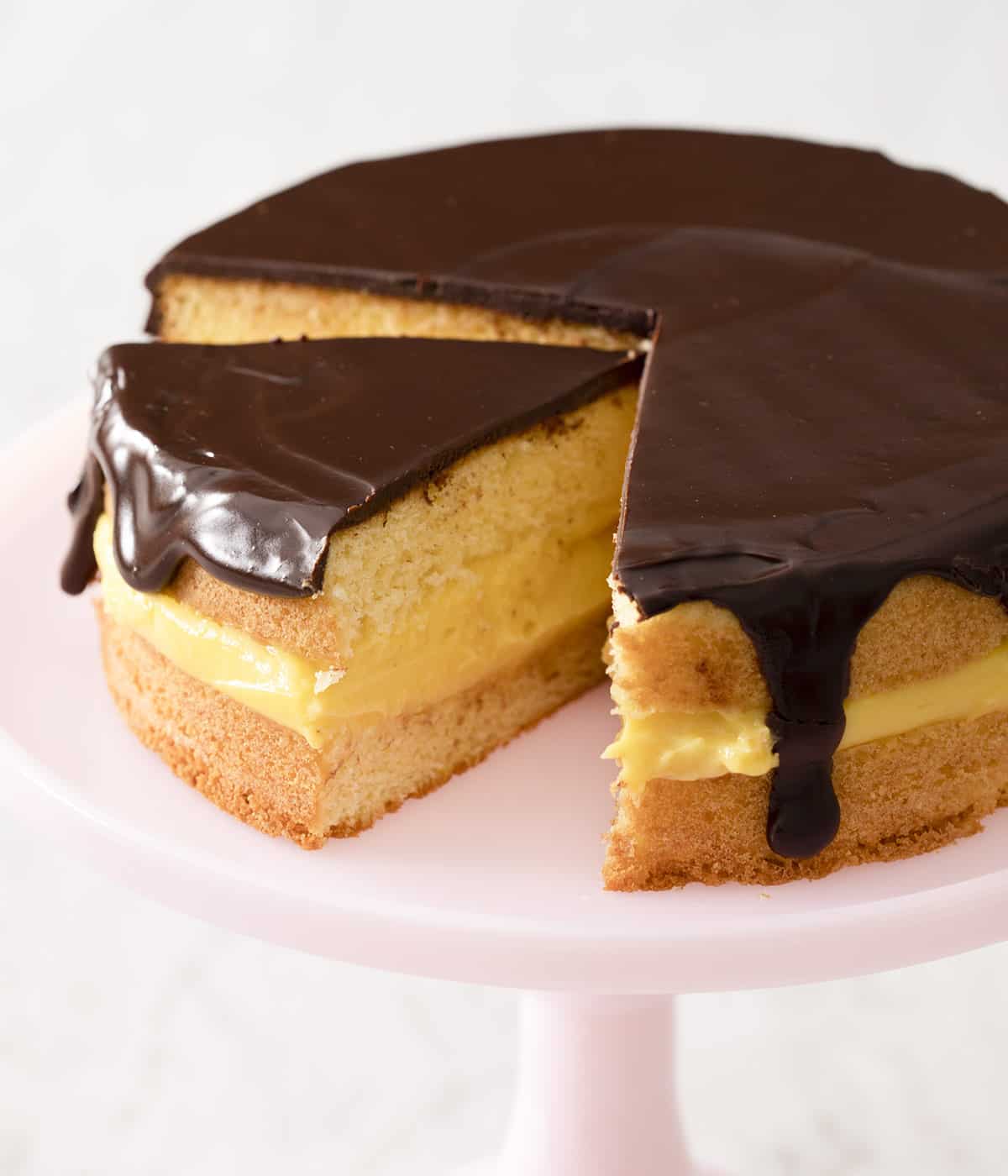 Boston cream pie with some pieces cut out on a cake stand.