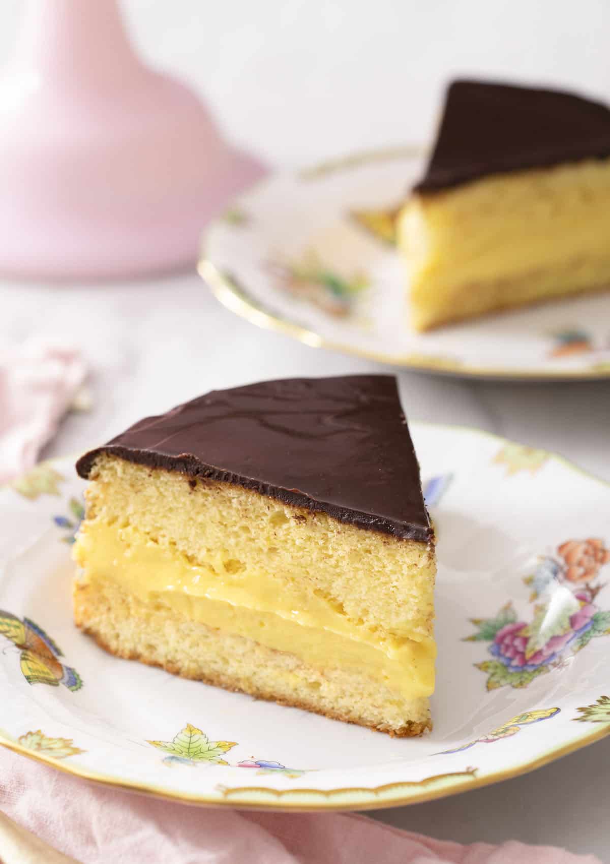 Two pieces of Boston cream pie on porcelain plates.