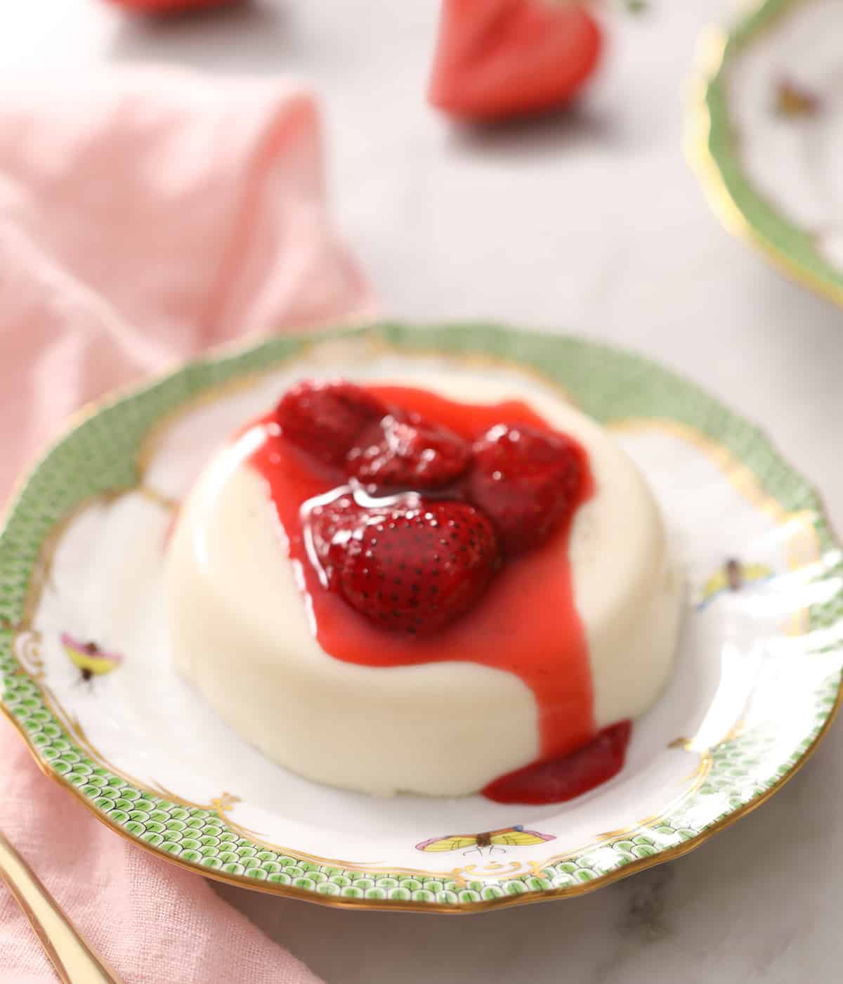 A panna cotta on a porcelaiin plate with strawberries on top. 