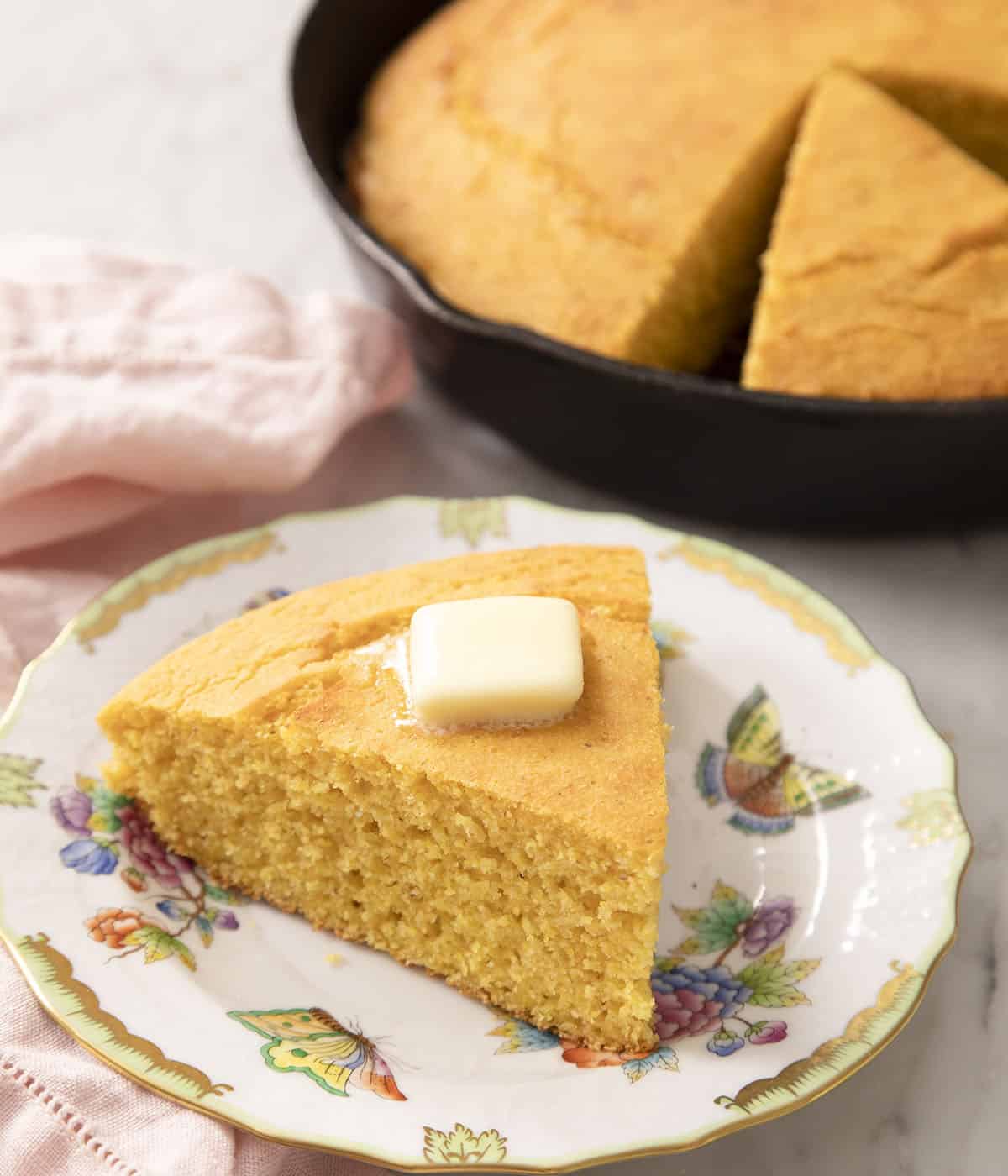 A wedgee-shaoped piece of cornbread on a plate in front of a round loaf.