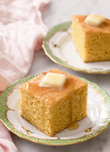 Pieces of cornbread topped with butter and honey on porcelain plates.