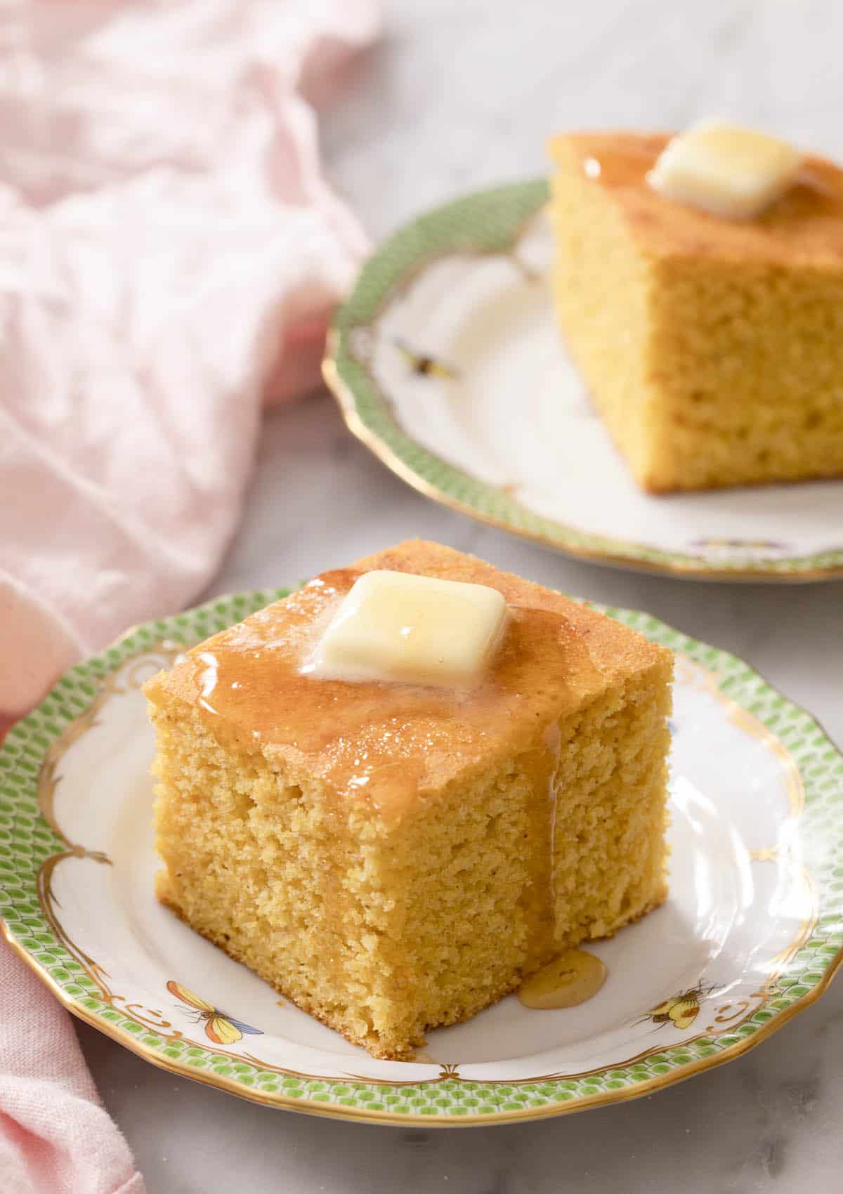 Pieces of cornbread topped with butter and honey on porcelain plates.