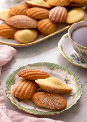 A green and white plate with Madeleines on a marble counter.