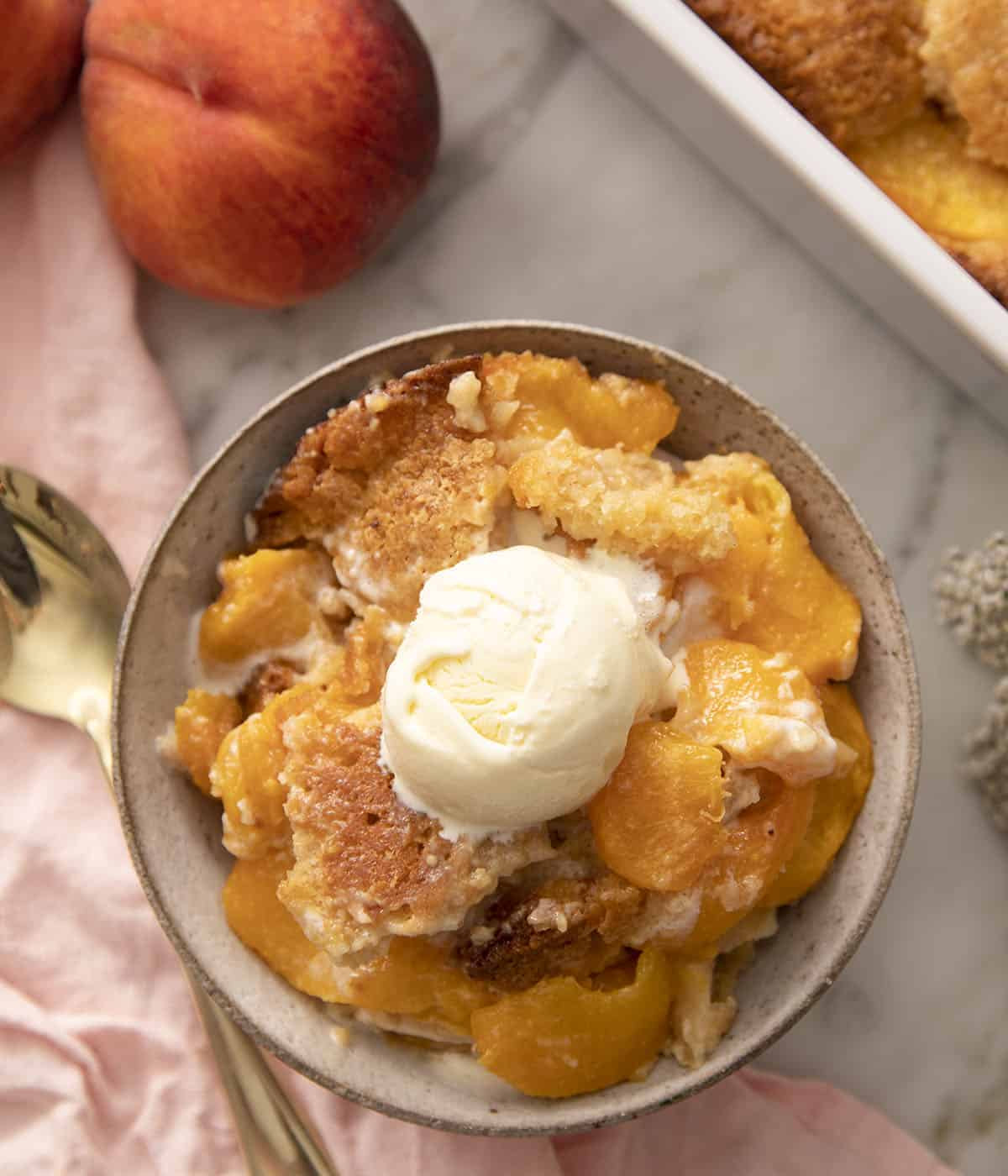 Peach cobbler in a grey bowl with ice cream.