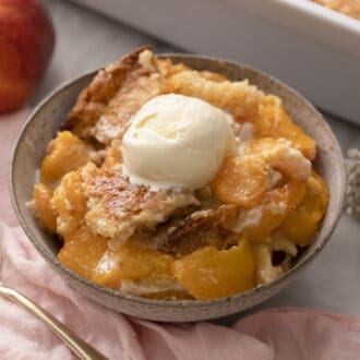 A bowl filled with peach cobbler and topped with vanilla ice cream.