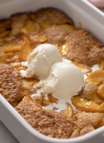A delicious peach cobbler topped with two scoops of vanilla ice cream.