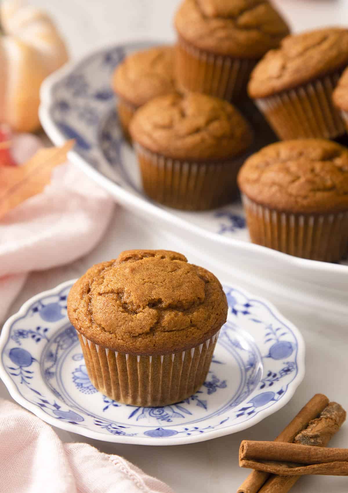 A pumpkin muffin on a blue and white plate next to cinnamon sticks.