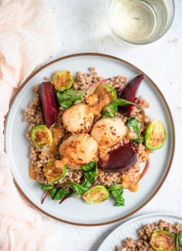An overhead shot of 3 sauteed scallops on a plate with cous cous and veggies