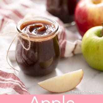 A glass containere filled with apple butter next to some apples.