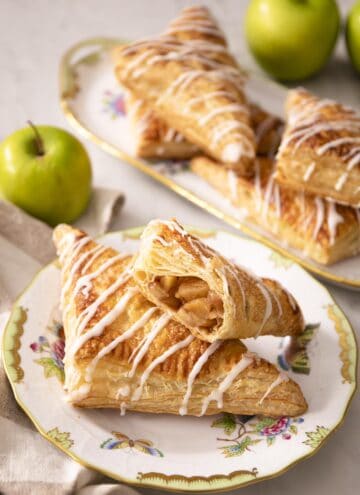 Apple turnovers on a porcelain plate next to green apples.
