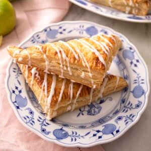 Two apple turnovers on a plate with glaze drizzled on top.