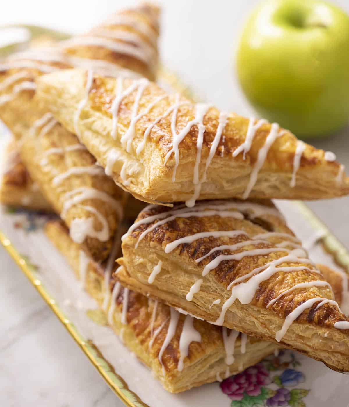A stack of apple turnovers on a platter next to a green apple.