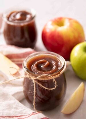 A glass jar with apple butter next to some apples.