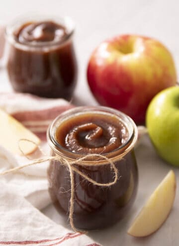 A glass jar with apple butter next to some apples.