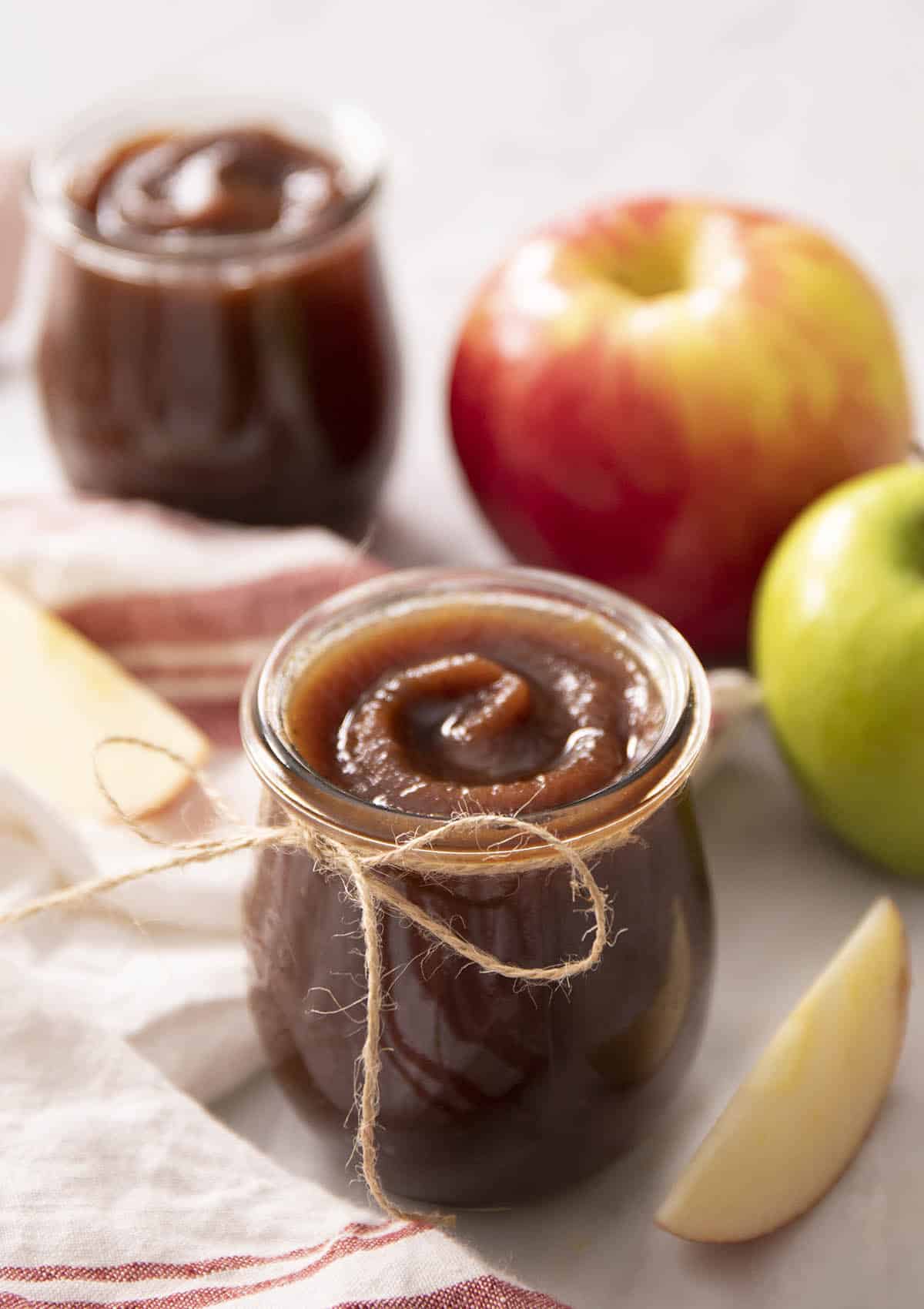 A glass jar with apple butter next to some apples.