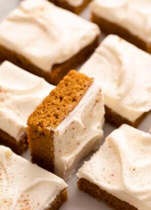 Pumpkin bars with cream cheese frosting on a marble counter.