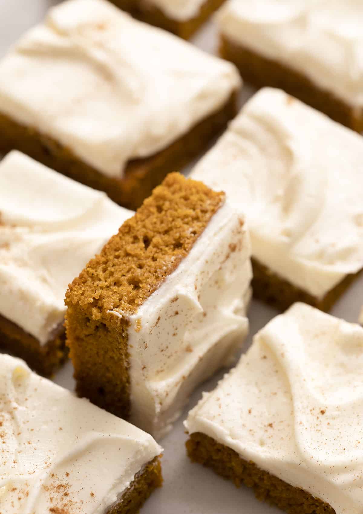 Pumpkin bars with cream cheese frosting on a marble counter.