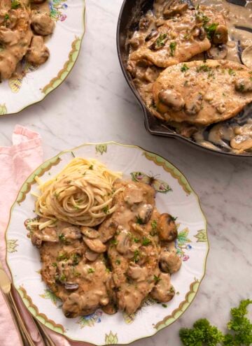 Two plates of chicken marsala on a marble counter.